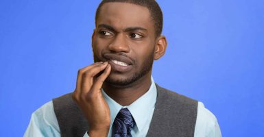 Closeup portrait handsome sad young executive man, student, worker touching face having bad pain, tooth ache, isolated blue background. Negative human emotions, facial expressions, feeling reaction