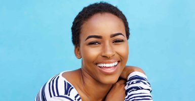 Close up portrait of beautiful young black fashion woman smiling against blue wall