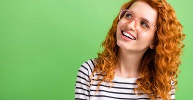 Photo of excited adorable young lady dressed striped clothes glasses smiling looking empty space isolated green color background.